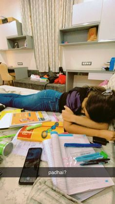 a woman laying on top of a bed covered in papers and pens next to a cell phone