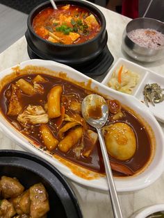 a table topped with different types of food and bowls filled with soup, meats, and veggies