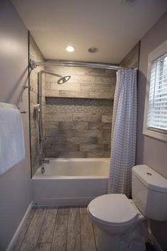 a white toilet sitting next to a bath tub under a window in a small bathroom