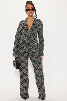 a woman standing in front of a white wall wearing black and grey plaid pantsuits