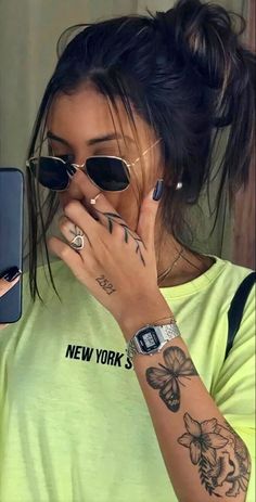 a woman with tattoos on her arm holding a cell phone to her face and looking at the screen