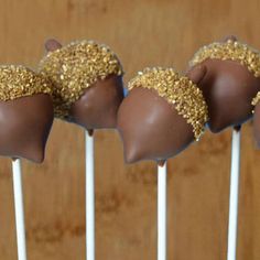 four chocolate covered candies with gold sprinkles on them sitting on top of white sticks