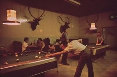 a group of people playing pool in a room with deer heads mounted on the wall