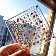 a person is holding up a glass box filled with small rocks in front of a window