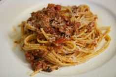 a white plate topped with spaghetti covered in sauce and ground meat on top of it