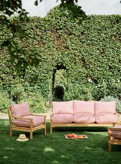 a couch and two chairs sitting on top of a grass covered field next to a hedge