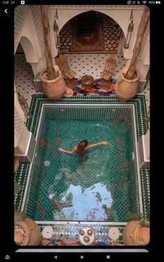 a woman swimming in a pool surrounded by tiled walls and pillars with columns on either side