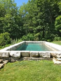 an outdoor swimming pool surrounded by rocks and grass in the middle of a wooded area