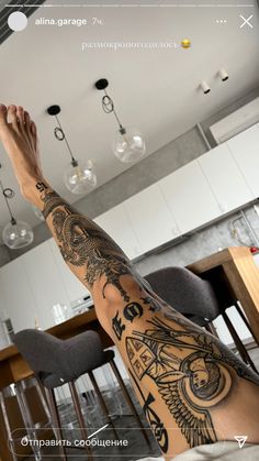 a man with tattoos on his legs and arms sitting in front of a kitchen counter