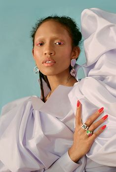 a woman in a white dress with her hands on her chest, wearing earrings and rings