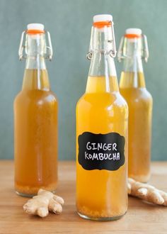 three glass bottles filled with ginger kombucha sitting on top of a wooden table