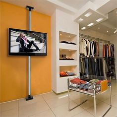 a television that is mounted to the wall in a closet with clothes on racks and an orange chair