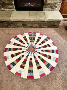 a circular quilt on the floor in front of a fireplace with a fire place mat