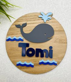 a wooden sign that says tomi with a whale on the front and blue water below it