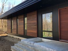 a modern house with wood siding and glass doors on the front door, steps leading up to it