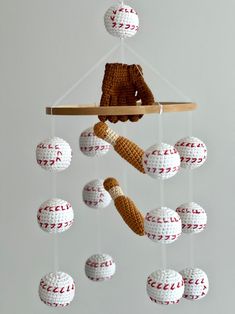 a crocheted teddy bear is hanging from a mobile with baseballs and balls