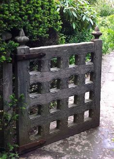 an old wooden gate surrounded by bushes and flowers on a path in the middle of a garden