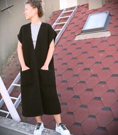 a woman standing in front of a red brick building wearing a black knitted vest