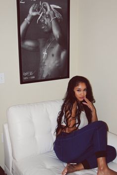 a woman sitting on top of a white couch in front of a wall mounted poster