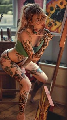 a woman with lots of tattoos on her body posing in front of a easel