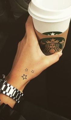 a woman's hand holding a starbucks cup with stars on the sleeve and wrist