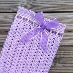 a purple crocheted bag with a bow on it sitting on a wooden surface