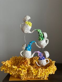 three white teapots on top of yellow and purple flowers with green stems in the middle