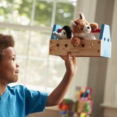 a young boy holding up a wooden toy with two stuffed animals on top of it