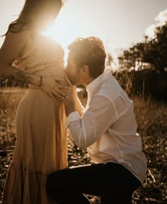 a man kneeling down next to a woman in a dress and holding her hand on her stomach