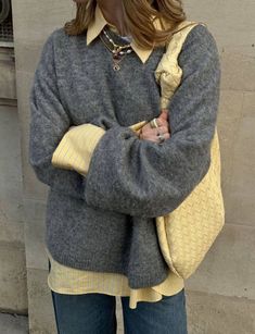 a woman standing in front of a building with her hand on her hip wearing a yellow and gray sweater