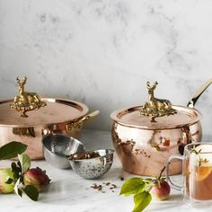 copper pots and pans on a marble countertop with apples in the foreground