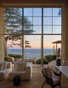 an open living room with large windows overlooking the ocean and trees in front of it