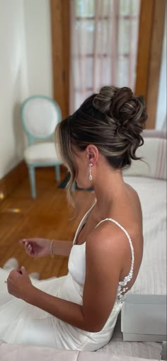 a woman sitting on top of a bed wearing a white dress and holding her hand out