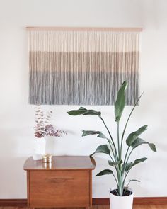 a potted plant sitting on top of a wooden table next to a wall hanging