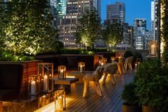 an outdoor deck is lit up with candles and greenery in the city at night