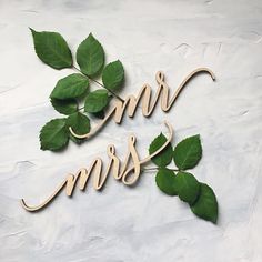 the word mr and mrs spelled with wooden letters surrounded by green leaves on a white surface