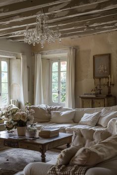 a living room filled with lots of furniture next to two windows and a chandelier