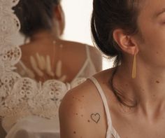 a woman with tattoos on her left arm looking at herself in the mirror while wearing a white top