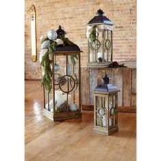 two metal lanterns with christmas decorations on them in front of a brick wall and wooden floor