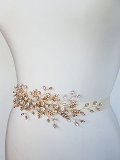 a bridal belt with pearls and leaves on it's side, sitting on a mannequin