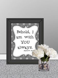 a vase filled with white flowers sitting next to a framed sign that says, behold i am with you always