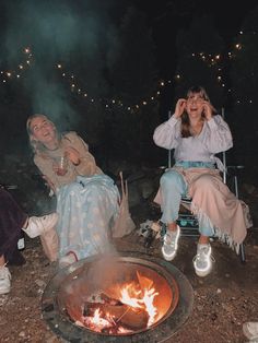 two women sitting around a campfire at night