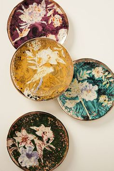 four plates with flowers painted on them sitting next to each other