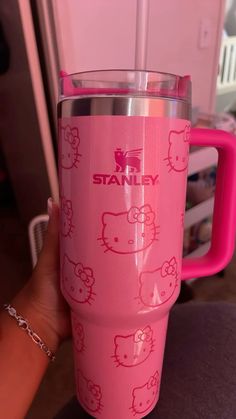 a pink hello kitty tumbler cup sitting on top of a table next to a person's hand