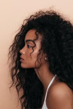 a woman with long curly hair wearing a white tank top looking off to the side