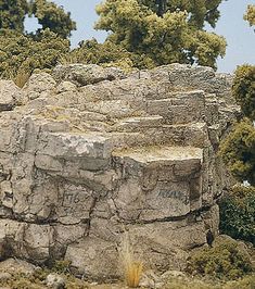 a giraffe standing on top of a rocky hill next to trees and bushes