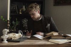 a man sitting at a table with books and a candle in front of him reading