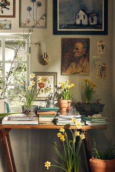 a table topped with lots of books and flowers next to a wall covered in pictures