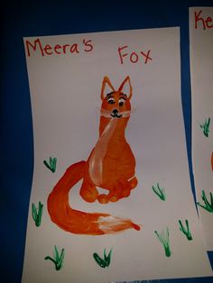 two children's handprints depicting foxes on paper with grass and carrots