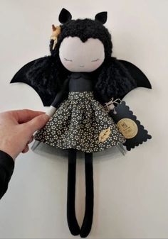 a hand holding a doll with black wings and a dress on it's body